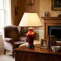 Oxblood ceramic table lamp with a cream shade on a wooden table in a classic living room.