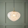 Art Deco pendant lamp with a white confetti glass shade and brass fixture hanging against a green paneled wall.