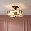 Square Tiffany ceiling light with geometric cream and grey glass panels glowing above pink wainscoted walls.