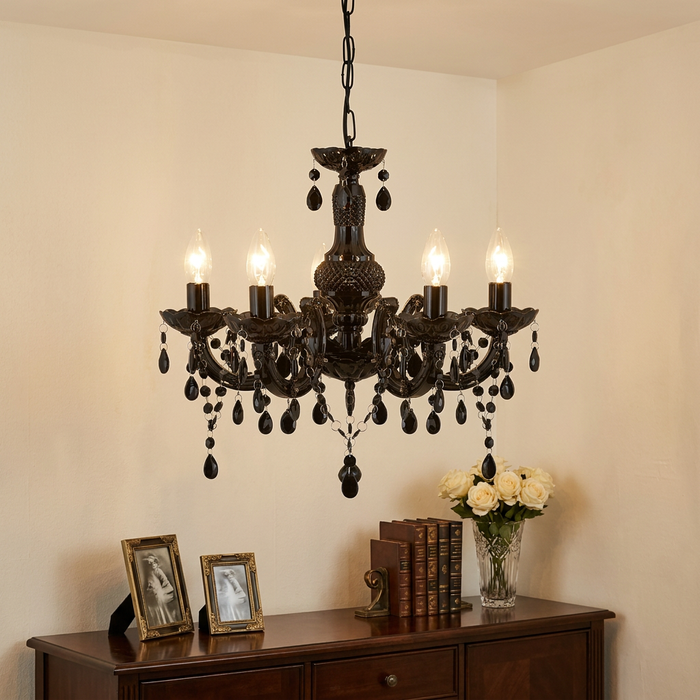 Five-light black Marie Therese chandelier with teardrop droplets hanging above a wooden sideboard with flowers.