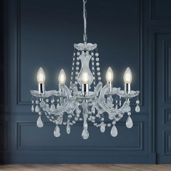 Marie Therese 5 light chrome and crystal glass chandelier with hanging droplets against a dark blue paneled wall.