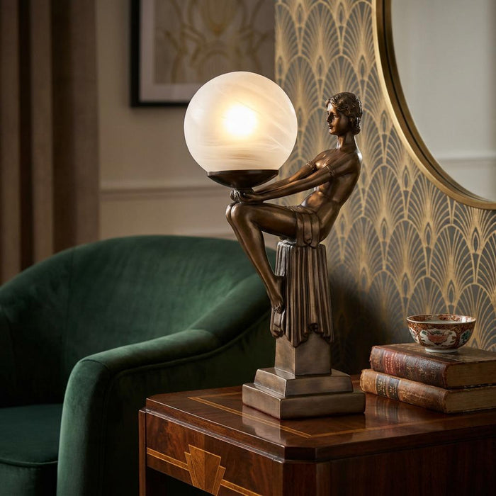 Bronze Art Deco figurine lamp of a woman holding a glowing glass globe on a mahogany side table.