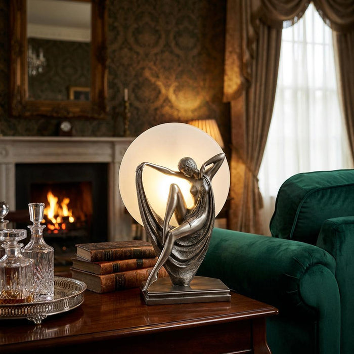 Art Deco figurine lamp with a silver female figure and glowing glass globe on a table in a cozy room.