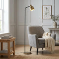 Mayfield Modern Brass Floor Lamp with a slender black stem and brass head next to a grey armchair in a living room.