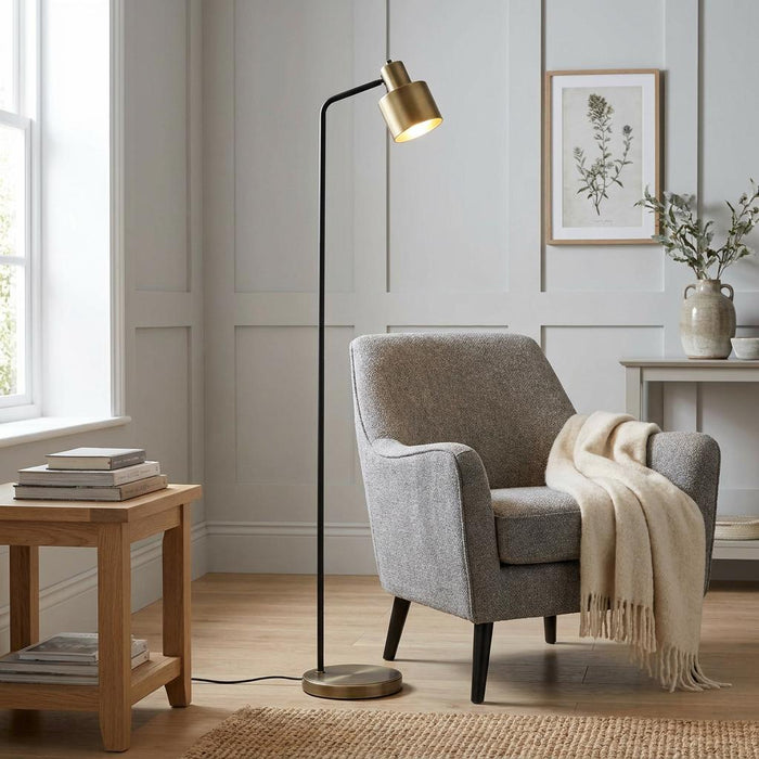 Mayfield Modern Brass Floor Lamp with a slender black stem and brass head next to a grey armchair in a living room.