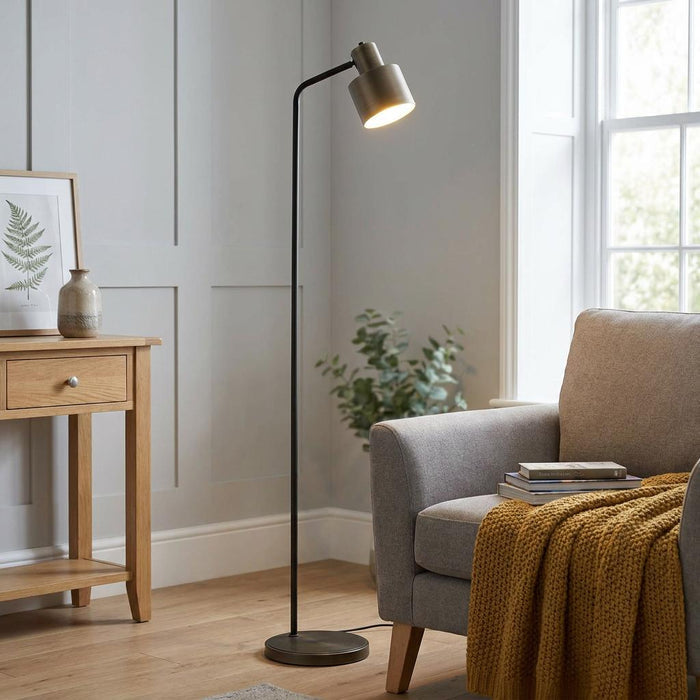 Mayfield Modern Bronze Floor Lamp with an angled shade lit next to a grey armchair in a neutral-toned room.