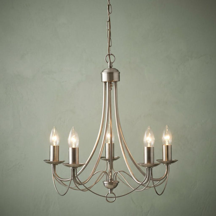 Elegant 5-light satin silver chandelier with lit candle bulbs against a pale green textured wall.