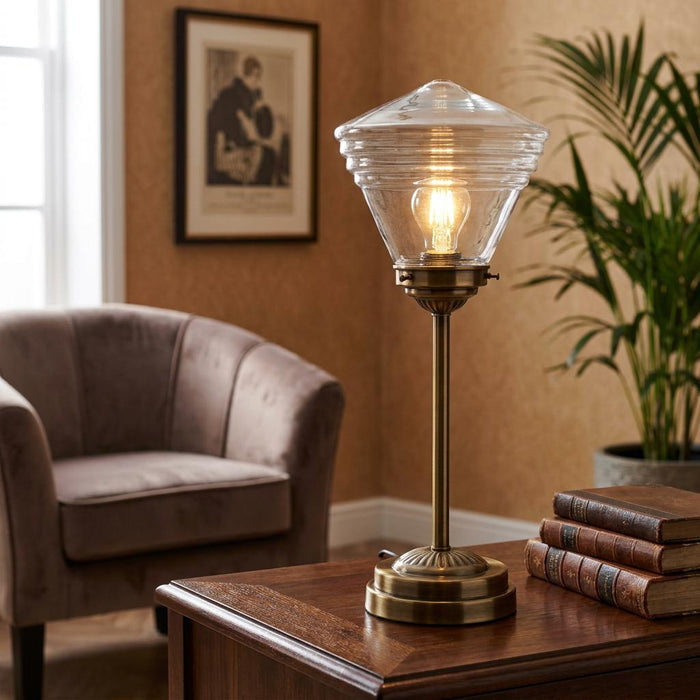 Medium brass table lamp with a clear ribbed glass shade on a wooden desk in a cozy room.