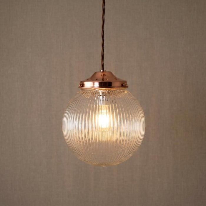 A lit prismatic glass globe pendant light with a copper gallery hangs against a neutral textured background.