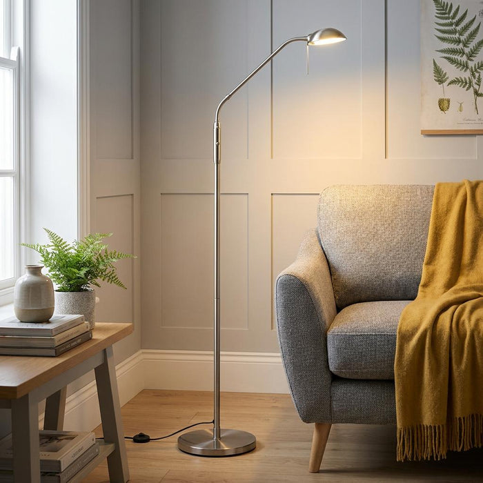A slim, antique chrome floor reading lamp with a curved arm illuminating a cozy living room chair.