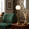 Mia Brass Art Deco Figurine Lamp with a frosted globe on a wooden side table next to a green geometric chair.