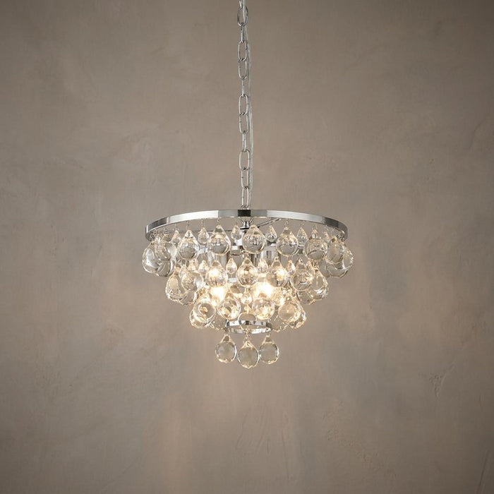 Lit 4-light chrome pendant featuring tiers of glass crystal droplets against a neutral textured wall.