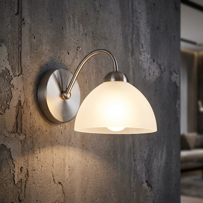 Milanese satin silver wall light with a glowing alabaster glass shade mounted on a rustic concrete wall.