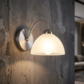 Milanese satin silver wall light with a glowing alabaster glass shade mounted on a rustic concrete wall.