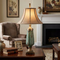 Green fluted ceramic table lamp with a warm beige bell shade on a wooden table in a cozy traditional living room.