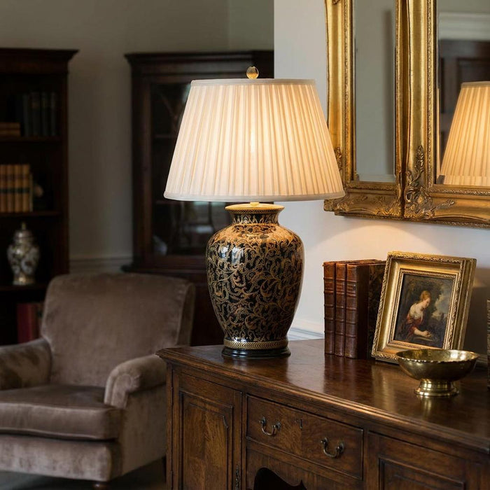 Morris table lamp with gold patterns and pleated shade on a wooden sideboard in a traditional living room.