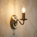 Antique brass wall light with a twisted arm and lit candle bulb on damask wallpaper.