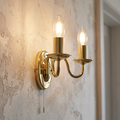 Oaks Nadoor two-light gold wall sconce with glowing candle bulbs on a textured plaster wall.