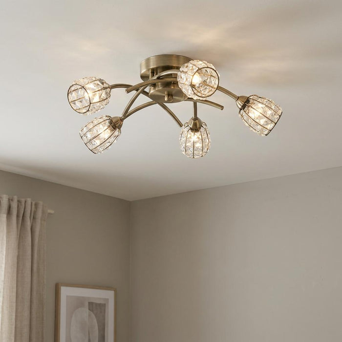 Naira 5-light antique brass flush ceiling light with crystal cage shades illuminated against a plain ceiling.