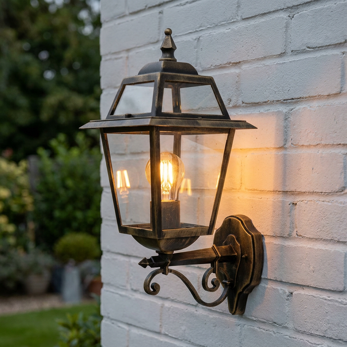 Traditional black and gold lantern wall light with a lit bulb mounted on a white brick wall.