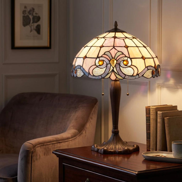 A glowing Tiffany table lamp with an ornate stained glass shade sits on a dark wood table next to old books.