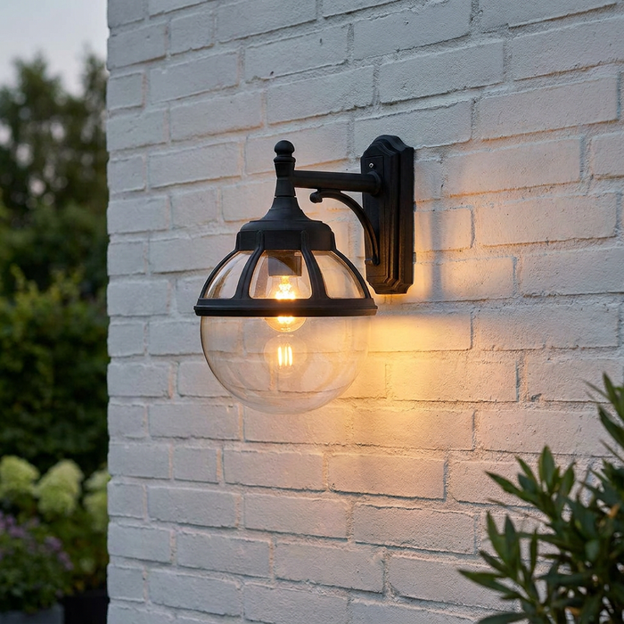Norlys Bologna black outdoor wall light with a clear glass globe mounted on a white brick wall, glowing warmly.