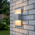 Modern aluminium outdoor wall light with up and down lighting and PIR sensor mounted on a white brick wall.