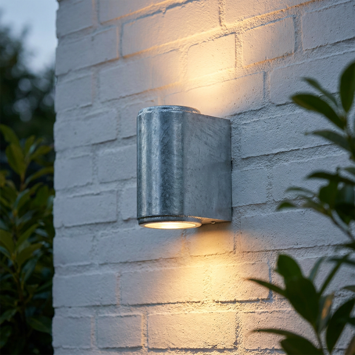 Galvanized outdoor wall light mounted on white brick, casting warm up and down light glows.