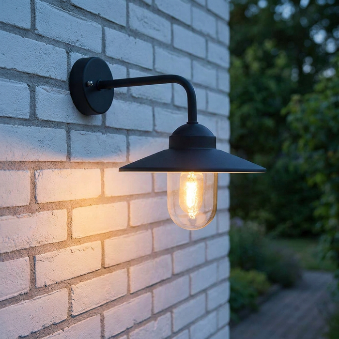 A black swan-neck outdoor wall light with a warm glowing bulb mounted on a white brick wall at dusk.