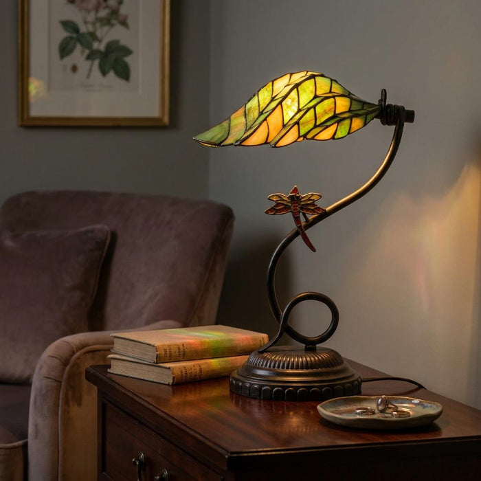 Tiffany table lamp with a green leaf-shaped shade and dragonfly detail on a wooden side table.