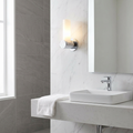 Oaks Afia chrome bathroom wall light with frosted glass cylinder shade on a marble wall beside a mirror.