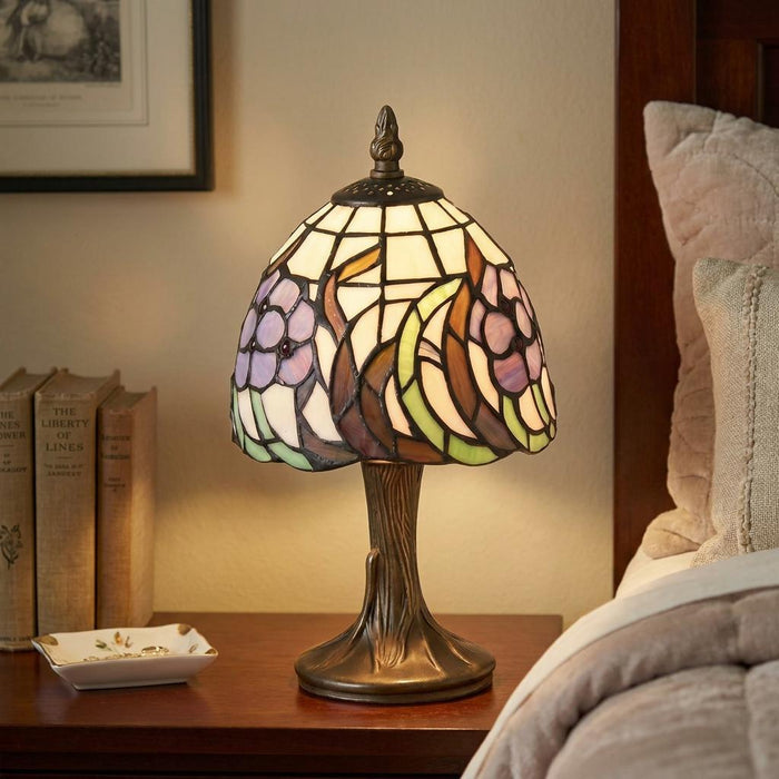 Tiffany-style bedside lamp with floral stained glass shade on a tree-trunk base, glowing on a wooden nightstand.