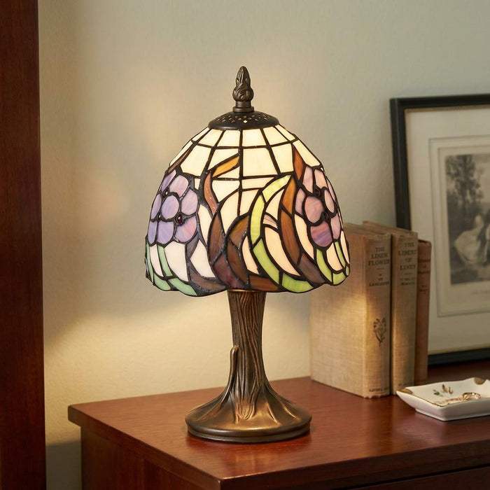 Tiffany bedside lamp with a floral stained glass shade and bronze tree-trunk base on a wooden surface.