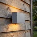 Silver-grey rectangular LED wall light on a wooden exterior wall, emitting a warm up and down glow.