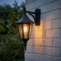 A traditional black outdoor lantern mounted on a white brick wall, emitting a warm glow from a filament bulb.