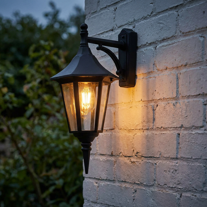 A traditional black outdoor lantern mounted on a white brick wall, emitting a warm glow from a filament bulb.