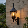 Traditional black lantern-style wall light with a warm glowing bulb mounted on a light brick wall.