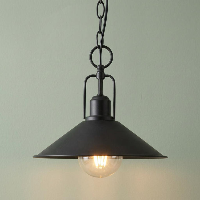 Industrial black pendant ceiling light with a wide metal shade and chain hanging against a pale green wall.