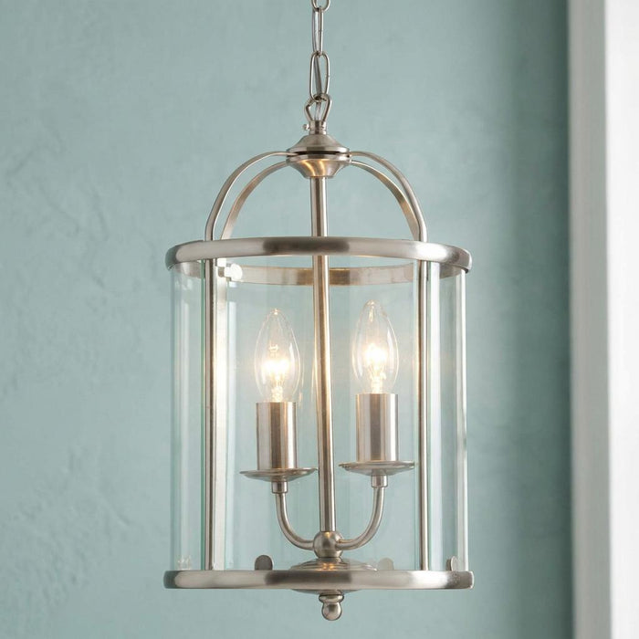 Antique chrome two-light ceiling lantern with a clear glass shade lit against a pale blue wall.