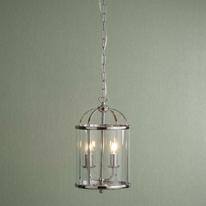 A 2-light chrome cylindrical lantern with clear glass panels hanging from a chain against a sage green wall.