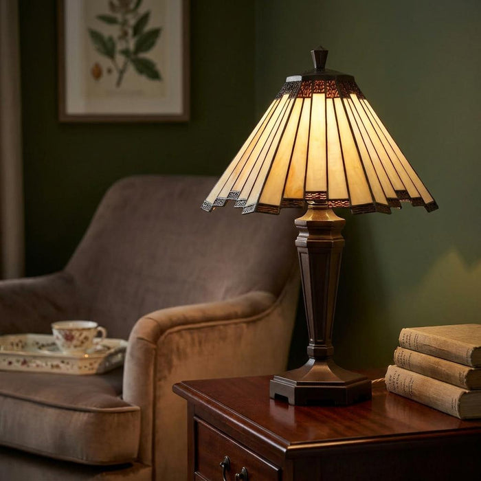 Lit Tiffany table lamp with a pleated cream glass shade on a dark wood table in a warm, cozy living room.