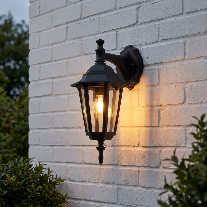 A traditional black outdoor downlighter wall lantern with a warm bulb glow, mounted on a white brick wall.