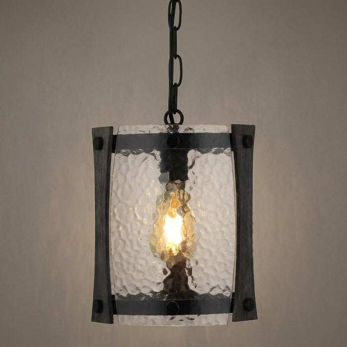 Black hanging lantern with textured glass panels and a single glowing light bulb against a neutral wall.