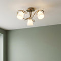 Antique brass semi-flush ceiling light with three white ribbed glass shades against a sage green wall.