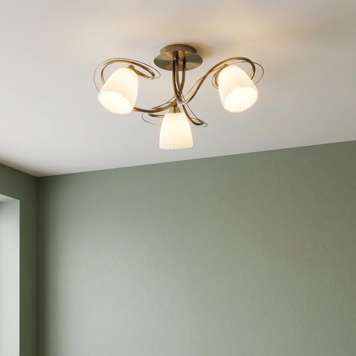 Antique brass semi-flush ceiling light with three white ribbed glass shades against a sage green wall.