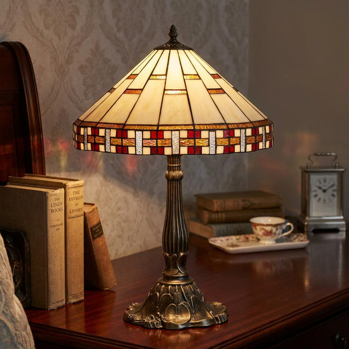 Aremisa Tiffany table lamp with a geometric cream and red glass shade on a wooden table next to books.