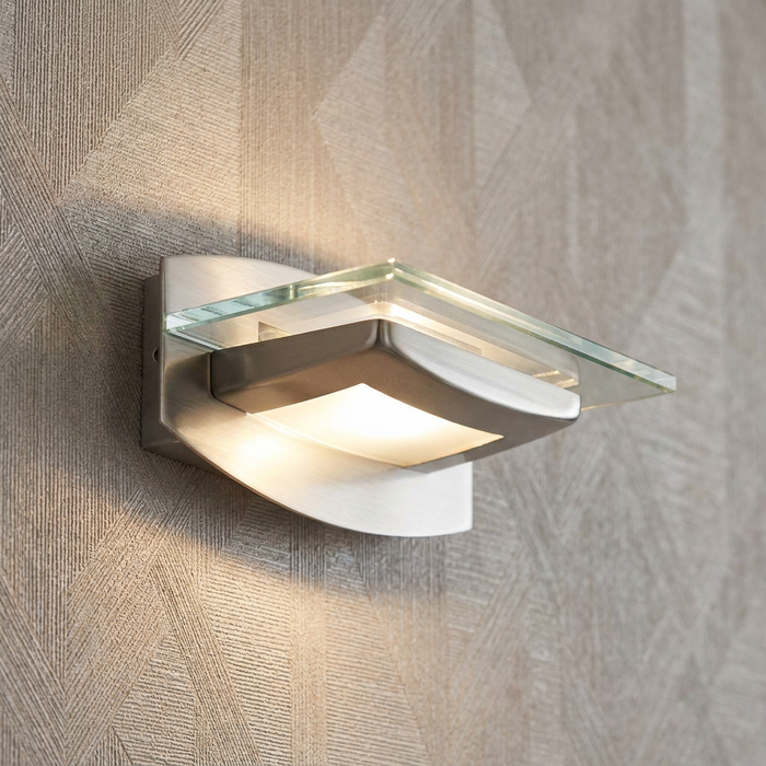 Illuminated Oaks Lighting Avia antique chrome wall light with a glass panel on a textured wall.