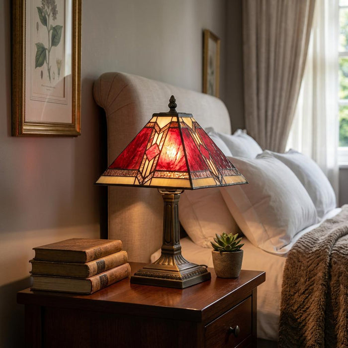 Aztec Tiffany bedside lamp with a red geometric shade on a nightstand in a cozy bedroom setting.