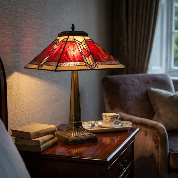 Aztec Tiffany table lamp with a red geometric shade glowing on a wooden bedside table in a cozy bedroom.