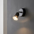Black single spotlight mounted on a grey wall, illuminated and angled downwards.